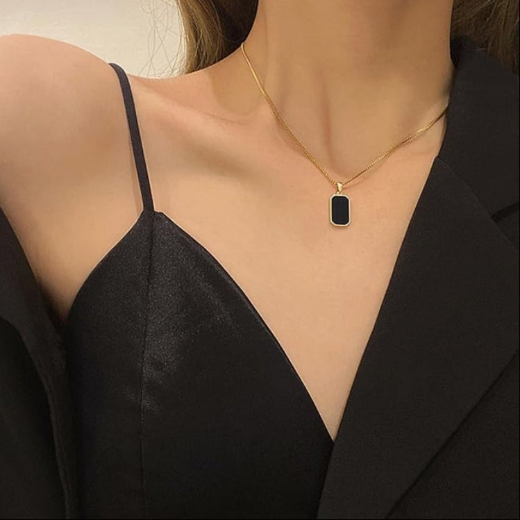 Gold necklace with a black pendant worn by a person in a black top.